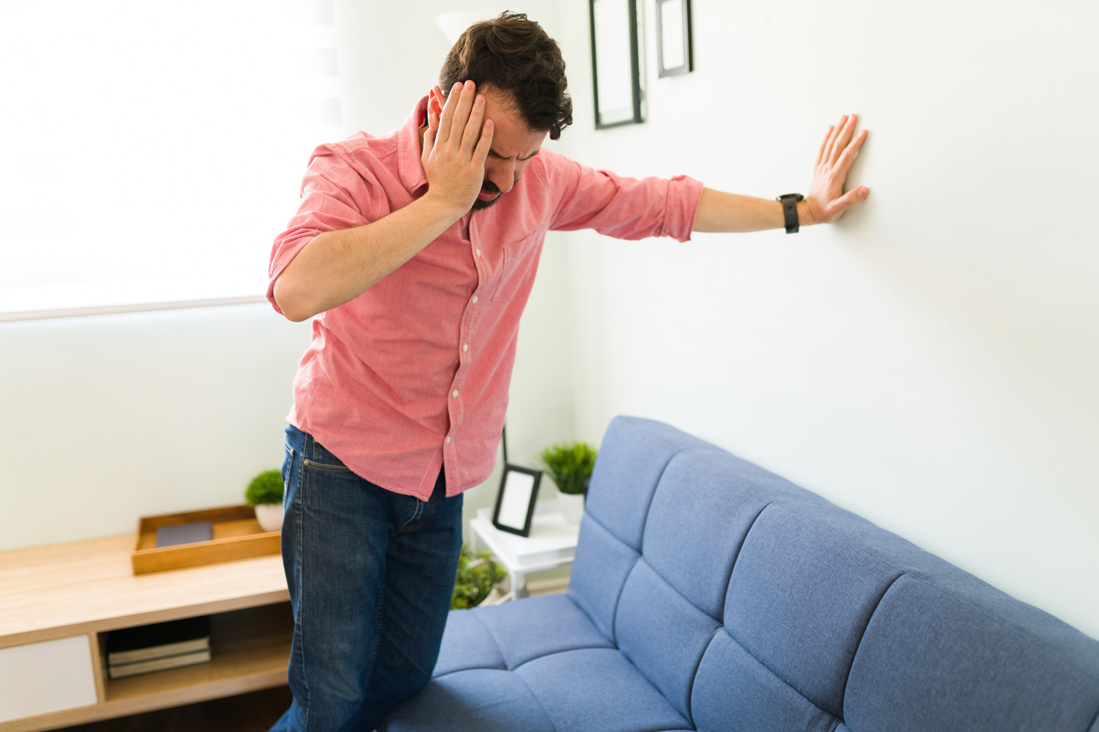 A man leaning against a wall holding one hand to his head